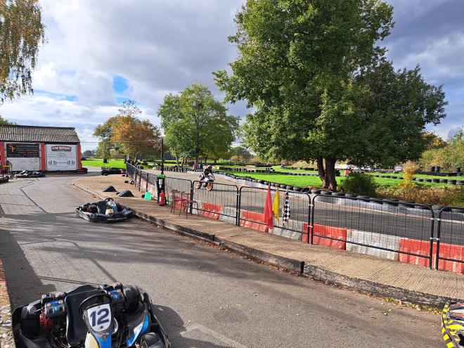 Motorbike riding around a karting track, with karts and the pit lane in the foreground.